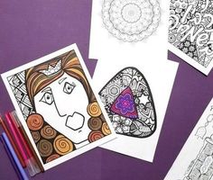 four coloring pages on a purple surface with markers and pencils next to them,