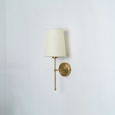 a wall light with a white shade on it's side and a lamp attached to the wall