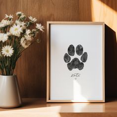 an animal paw print is displayed in front of a vase with daisies on the table