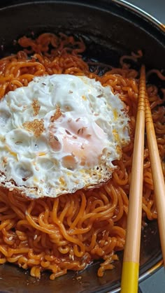 an egg sits on top of noodles in a skillet with chopsticks next to it