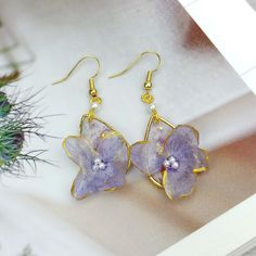 a pair of purple flower earrings sitting on top of a white table next to a potted plant