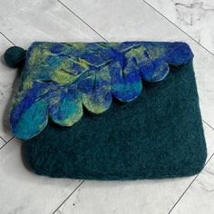 a green and blue purse sitting on top of a white tile floor next to a plant