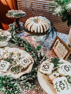 a table topped with lots of cookies and desserts next to a window covered in greenery