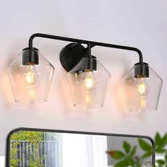 three light bathroom fixture with clear glass shades and black metal frame, on a white wall