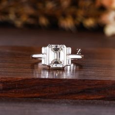 an emerald cut diamond ring sitting on top of a wooden table