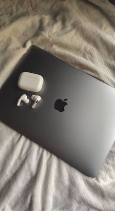 an apple laptop and ear buds on a bed