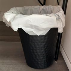 a black trash can sitting on the floor next to a stair case with white paper in it