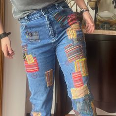 a woman standing in front of a mirror wearing blue jeans with colorful patches on them