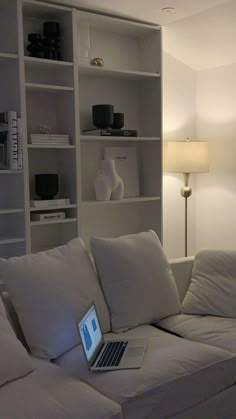 a laptop computer sitting on top of a couch in front of a white bookcase