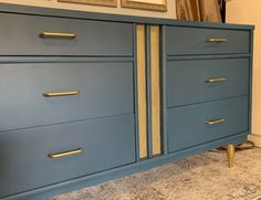 a blue dresser with gold handles in a living room or dining room area next to a painting on the wall