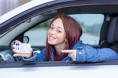 a woman sitting in the driver's seat of a car pointing at her identification card