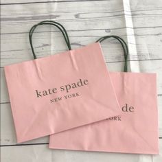 two pink shopping bags with the words kate spade and new york written on them sitting on a white wooden surface