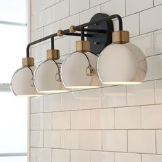 a bathroom light fixture with four lights on the side of it and a brick wall behind it