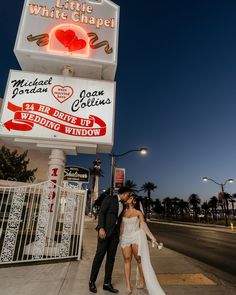 a bride and groom kissing in front of a white chapel sign at night with the lights on