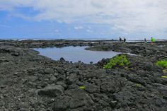 some people are standing on rocks by the water and looking out at the land that is covered in lava