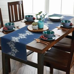 a wooden table topped with blue plates and bowls filled with fruit next to a potted plant