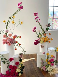 three white vases filled with flowers on top of a wooden floor