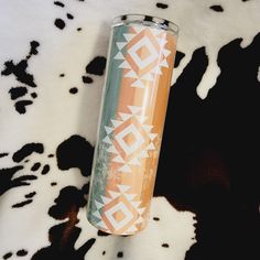 an orange and white tumbler sitting on top of a cow print rug with black spots