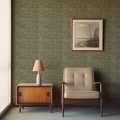 a chair sitting next to a table with a lamp on it in front of a painting