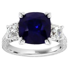 This Platinum Art Deco Estate ring features a 5.66 Carat Royal Blue Natural Antique Cushion shape Sapphire GIA Certificate 5201103617. Flanked by two old-mine cut diamonds weighing 1.16 Carat GIA certificates 5191781639 and 5191590933. The sapphire exhibit an excellent luster. A delicate etching is decorating this magnificent ring.