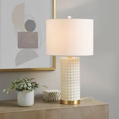 a white lamp sitting on top of a wooden table next to a potted plant