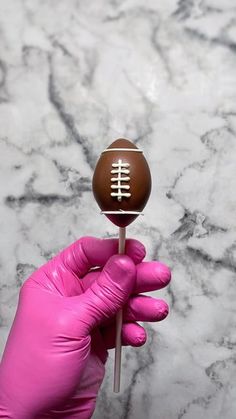 a person in pink gloves holding up a chocolate football on a toothpick with the word'football'painted on it