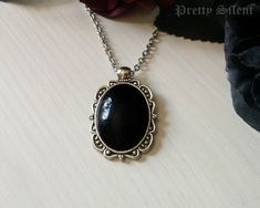 Handmade elegant, gothic style necklace  featuring a deep black glass cabochon that sits in a detailed antique silver ornate frame. Pendant size: 40 x 24 mm Cabochon size: 18 x 25 mm The necklace length can be chosen in the drop down menu.  Material: Antique silver plated metal alloy, glass cabochon All items come beautifully packaged. **PLEASE NOTE** : Standard Shipping is untracked to keep the shipping costs low. If you want to TRACK YOUR ORDER please select the SHIPPING UPGRADE at checkout! I