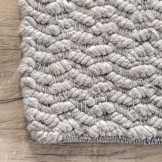 the textured rug is made from wool and has been placed on top of a wooden floor