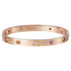 The 18k rose gold 10 multi-gem set Love bangle bracelet by Cartier is a true testament to the brand's exquisite craftsmanship and iconic design. This stunning bangle is adorned with a vibrant array of gemstones, including yellow and pink sapphires, green and orange garnets, and amethysts, creating a kaleidoscope of colors that captures the eye. Each gemstone is meticulously set in a rubover setting, ensuring their brilliance and allowing them to shine from every angle. The combination of rose gold and the vivid gemstones creates a captivating and harmonious contrast, resulting in a piece that exudes elegance and sophistication. This Love bangle is not only a beautiful accessory but also a symbol of commitment and enduring love. It comes complete with a screwdriver, allowing for easy and se Jewellery Cartier, Bracelets Cartier, Cartier Bangle, Cartier Jewellery, Garnet Jewellery, Amethyst Jewellery, Jewelry Cartier, Pink Gold Jewelry, Sapphire Bangle