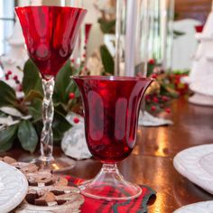 two red wine glasses sitting on top of a wooden table next to plates and cookies