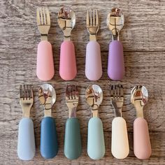 six different colored utensils are arranged in a row on a wooden surface with forks and spoons