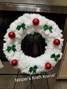 a white wreath with red balls and green bows on it, sitting in front of an oven