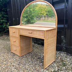 a wicker desk with a mirror on it in front of a black shipping container