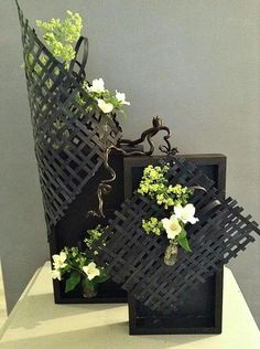 two black vases with flowers in them on a white counter top next to a gray wall