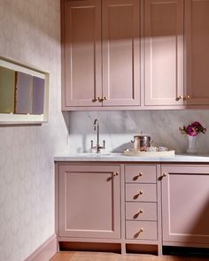 a kitchen with pink cabinets and white counter tops, along with a vase filled with flowers