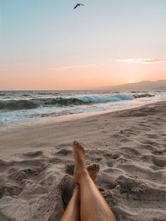 a person laying on the beach with their feet in the sand