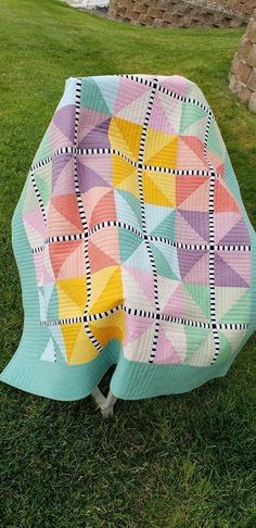 a colorful quilt sitting on top of a lush green field