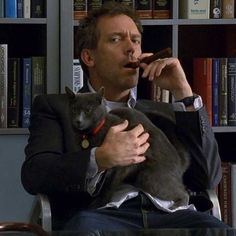 a man sitting in a chair holding a cat and talking on the phone with his mouth open