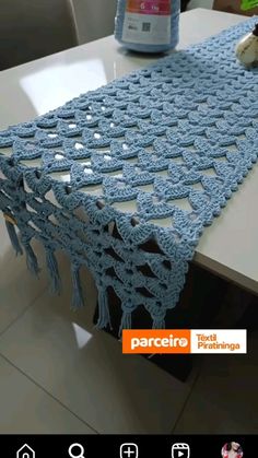 a crocheted table runner sitting on top of a white table next to a bottle of water