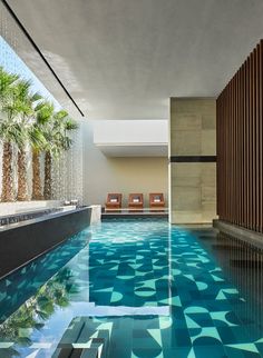 an indoor swimming pool with blue water and palm trees in the backgrouds