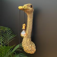 an ostrich lamp hanging from the side of a wall next to a plant