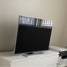 a flat screen tv sitting on top of a white dresser next to a printer machine