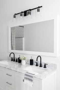 a white bathroom with two sinks and a large mirror above the sink is lit by three lights