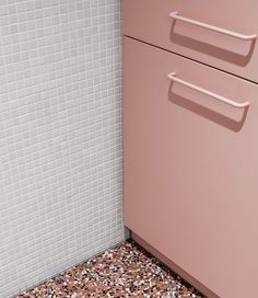 a bathroom with a pink cabinet and white tiled wall next to the toilet seat area