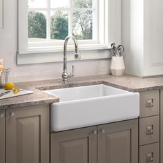 a white kitchen sink sitting under a window next to a counter top with fruit on it