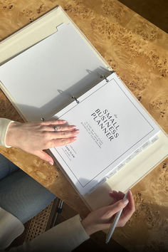 a woman is holding a pen and looking at a piece of paper on a table