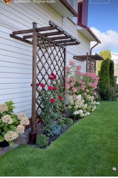 some flowers and plants in front of a house with a trellis on the side