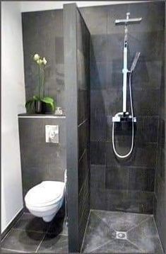 a bathroom with a toilet, shower head and black tile flooring in the corner