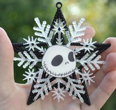 a hand holding a snowflake shaped ornament with a skull on it