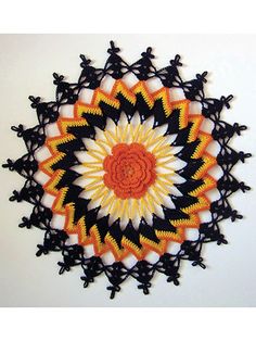 an orange and black crochet doily on a white wall with the sun in the center